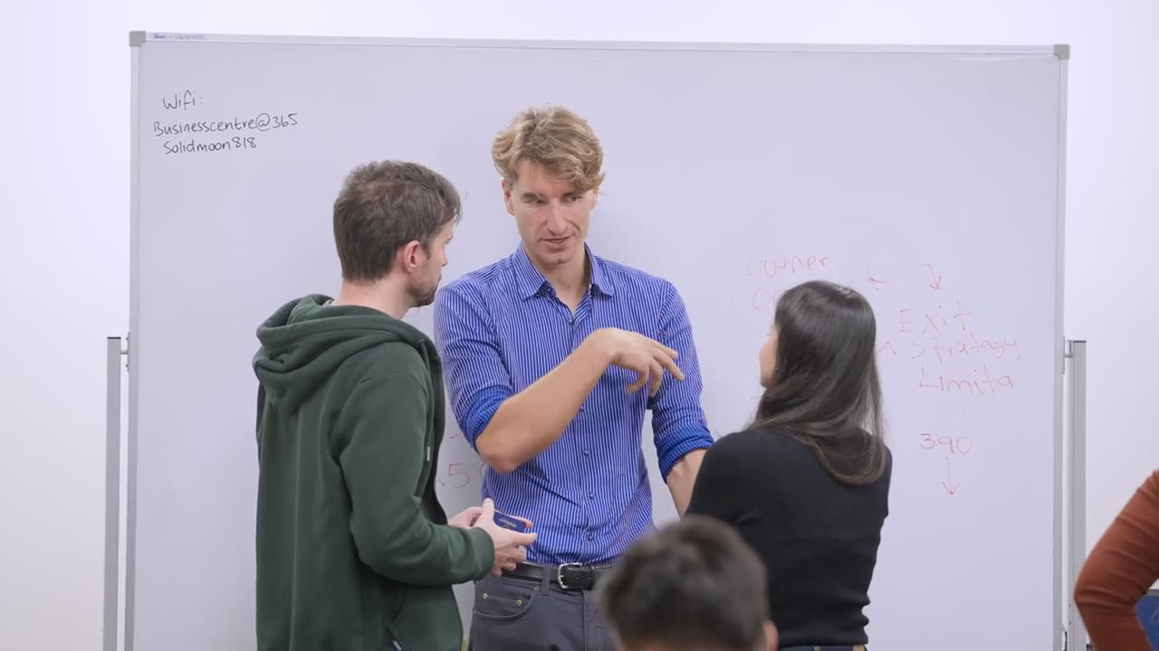 Christian Baumann explicando estrategia de salida y limitaciones en el pizarrón a dos asistentes